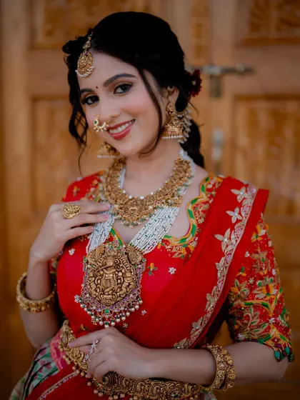 A joyful close-up portrait of a model in a bridal half saree. Her smile and the intricate details of the temple jewelry create a warm and inviting image for a wedding collection.