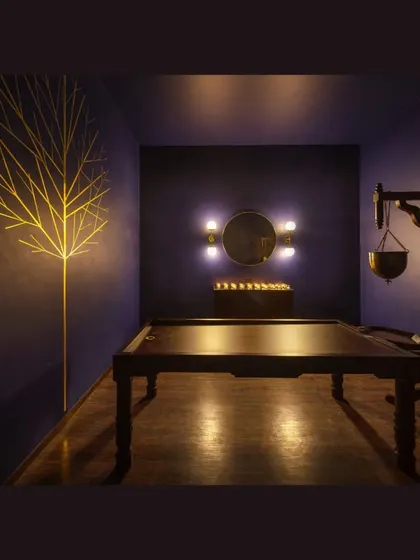 The spa treatment room, designed as a dark, cocoon-like space for ultimate relaxation. A brass Bodhi tree art installation provides a soft glow, enhancing the meditative quality.