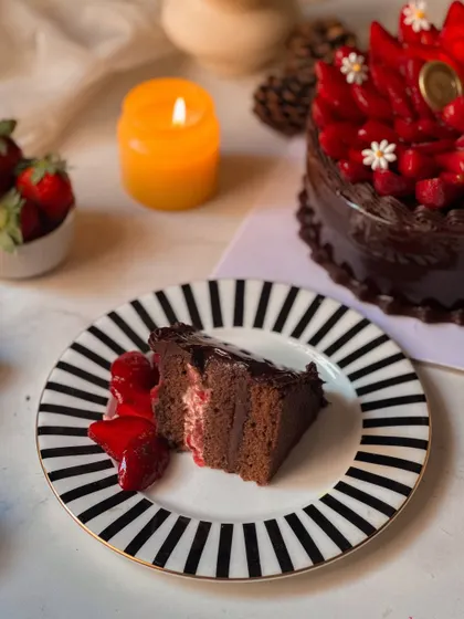 A slice of our Chocolate Strawberry Cake on a striped plate, accompanied by fresh strawberries. This shot emphasizes the rich, dark quality of the cake against the bright red of the fruit.