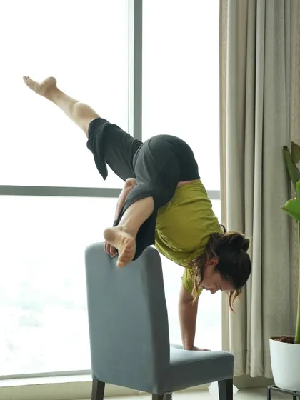 Using a chair to practice an arm balance, showing how everyday objects can be incorporated into your practice to build strength.