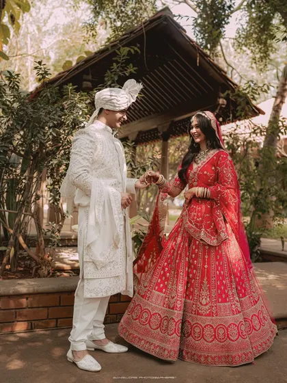 A grand portrait of the couple in their stunning wedding attire. The groom in his white sherwani and the bride in her red lehenga create a classic and regal picture.