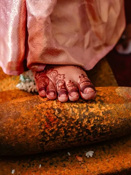 A detail shot of a traditional wedding ritual, where the bride's foot, adorned with henna, is placed on a grinding stone. We capture all the symbolic details.