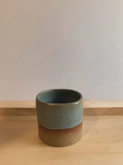 A two-toned mug with a soft blue-green glaze over a rustic terracotta-colored base. This simple, elegant piece is perfect for your daily coffee or tea.