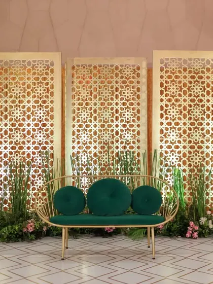 A chic and modern stage design featuring gold jaali panels and a stylish emerald green sofa. This setup blends traditional patterns with contemporary aesthetics for a unique look.