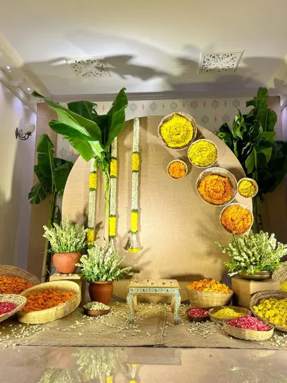 A simple and traditional Haldi setup with a backdrop of banana leaves and bowls of flower petals.