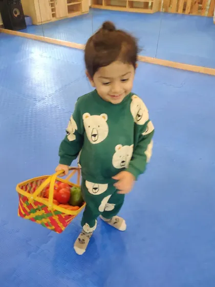 A happy shopper! This child walks with his basket of play vegetables, practicing real-life scenarios through role-play.