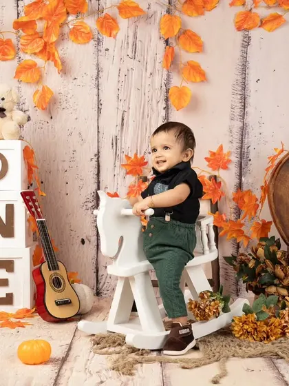 Clapping with joy for his first birthday. This autumn-themed setup with rustic wood and orange leaves creates a warm and cozy atmosphere for a celebration.