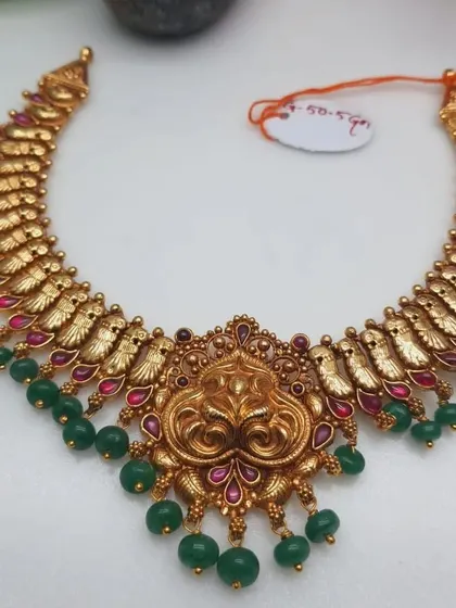 A beautiful temple necklace with a unique design, featuring a lion-faced pendant. The necklace is made from 92.5 silver with gold plating and is finished with green bead drops.