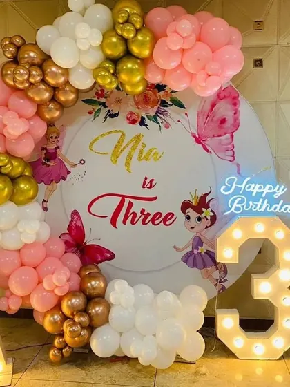 A fairy-themed third birthday party with a custom backdrop and a pink, gold, and white balloon arch.