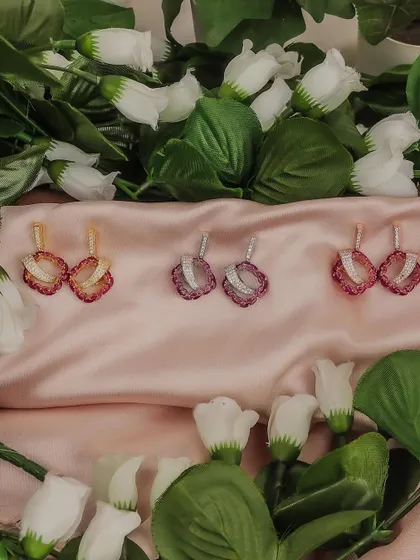 A creative product shot of shell-shaped earrings, nestled among white flowers on a pink satin cloth. This romantic styling is perfect for social media marketing and product showcases.