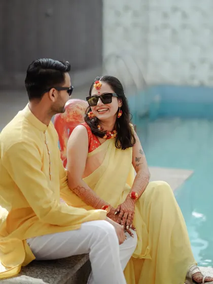 A candid moment of a couple sharing a laugh by the pool during their Haldi function. Their sunglasses and relaxed smiles give this shot a cool, modern vibe.