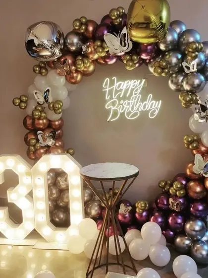 A glamorous 30th birthday with a circular balloon arch in chrome, metallic, and white balloons, accented with butterflies and a '30' marquee light.