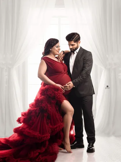 A sophisticated couple portrait against a bright window backdrop. The client's dramatic red gown contrasts beautifully with her partner's dark suit, creating a powerful and elegant image.