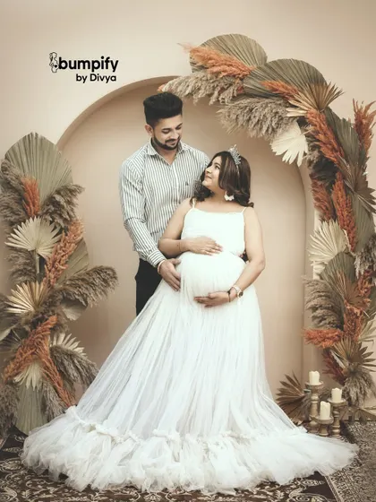 A loving glance between partners during a maternity photoshoot. The boho chic studio setup with pampas grass adds a soft, romantic texture to the moment.