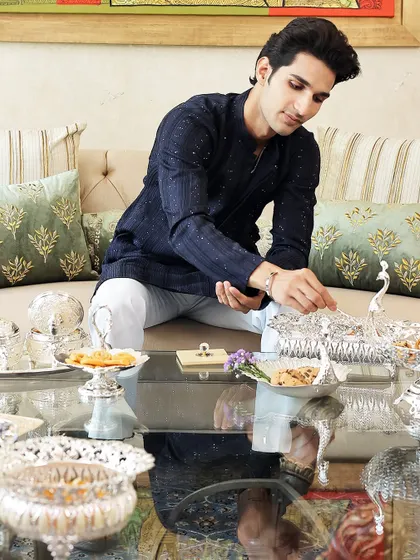Here, a guest enjoys the elegance of my silver-plated serveware. The intricate peacock and elephant motifs on the bowls and trays are designed to make hosting feel effortless and every celebration special.