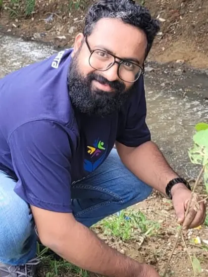 A volunteer from NTT Data proudly kneels by the sapling he just planted, contributing to the health of the Aravali Creek ecosystem.