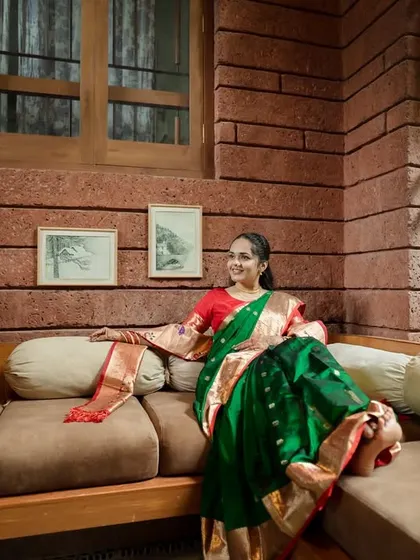 A relaxed and poised portrait of the bride, comfortably seated in a modern-rustic room that complements her beautiful green and red saree.