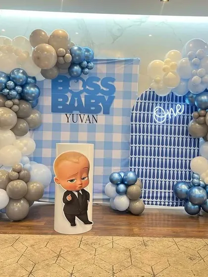 A Boss Baby themed first birthday with a blue and white gingham backdrop. The setup is framed by a balloon garland in grey, white, and blue chrome balloons.