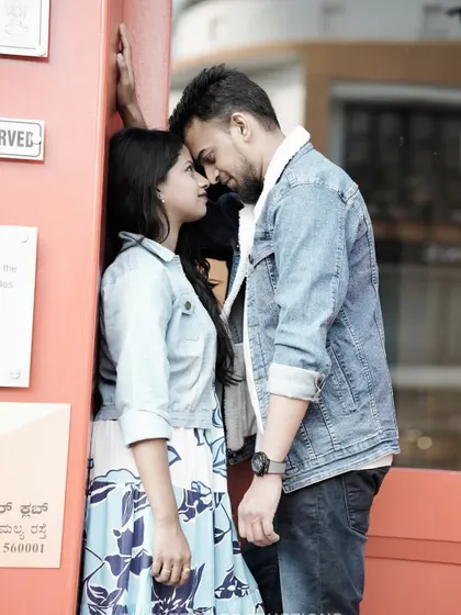 An intimate close-up of a couple, their foreheads touching, against a red wall, capturing a quiet moment in a busy urban setting.