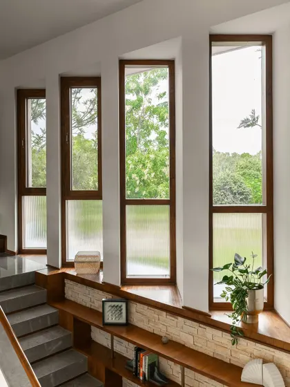 A series of tall windows along a staircase frames views of the lush greenery outside. The lower half features fluted glass to provide privacy without sacrificing the flow of natural light into the home.