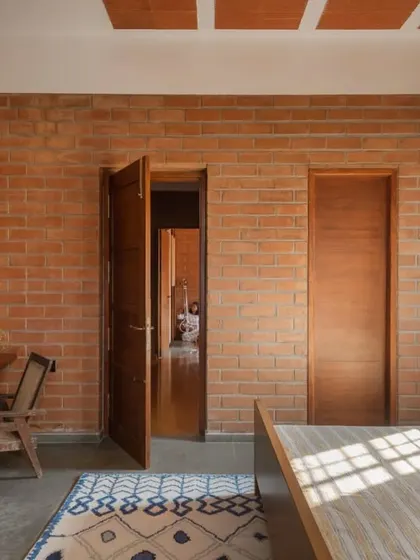 This bedroom in the Madhura house features exposed brick walls, a filler slab ceiling, and a built-in wooden study nook, combining rustic materials with functional design.
