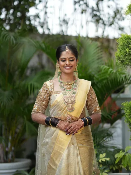 A bride looking serene in a beautiful cream-colored saree with a custom embroidered blouse and a sheer veil.