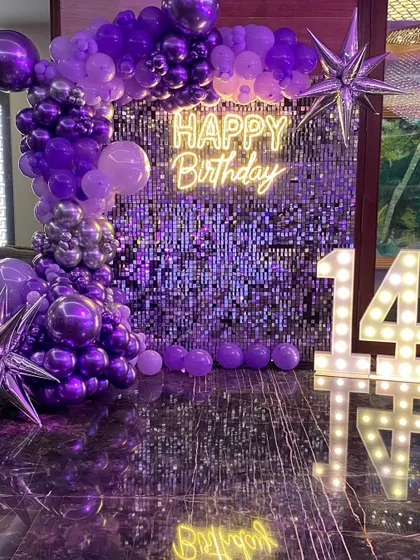 This is a duplicate of ID 64, 115, 129, 145, 196. A glamorous 14th birthday setup with a purple shimmer wall. This decoration features a stunning organic balloon garland in shades of purple and silver, a 'Happy Birthday' neon sign, and large marquee numbers.