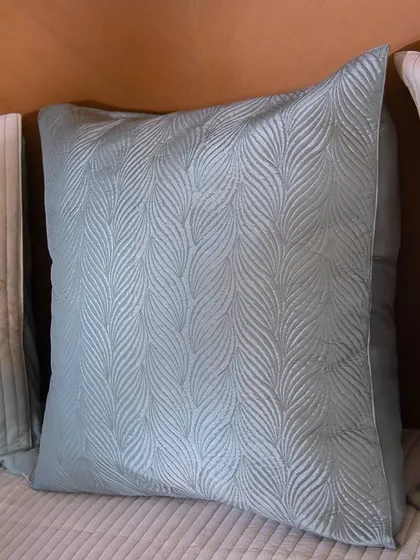 This close-up of a cushion showcases a beautiful, textured wave pattern in a soft, dusty blue. It's a design that speaks of quiet elegance and is perfect for a serene living space.