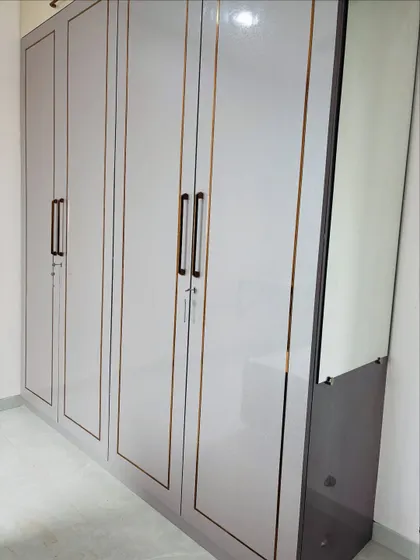 A full-height wardrobe with a light grey high-gloss finish and elegant gold-toned inlay. The attached dressing mirror makes the unit even more functional.