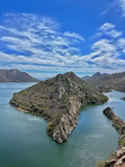 A panoramic view from Bahubali Hills in Udaipur, showing the stunning landscape of Badi Lake and the Aravalli ranges under a beautiful sky.