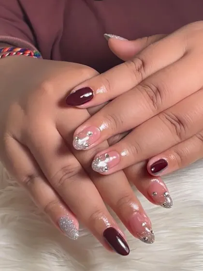 A glamorous party-ready set, combining a deep maroon polish with accent nails in sparkling silver glitter and rhinestones.