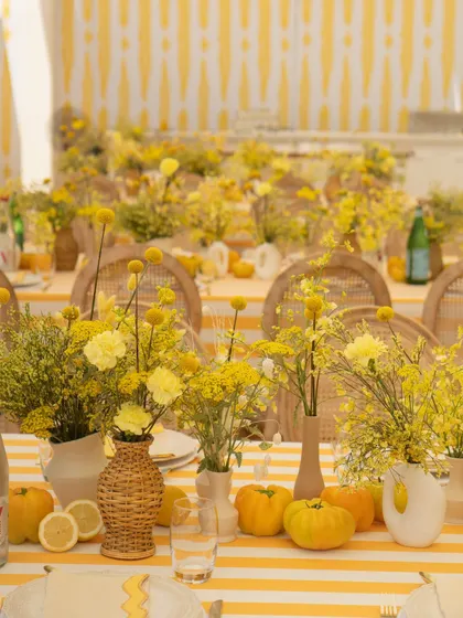 A long view of the dining tables, showing the cohesive design with striped tablecloths, rattan chairs, and an abundance of yellow florals.