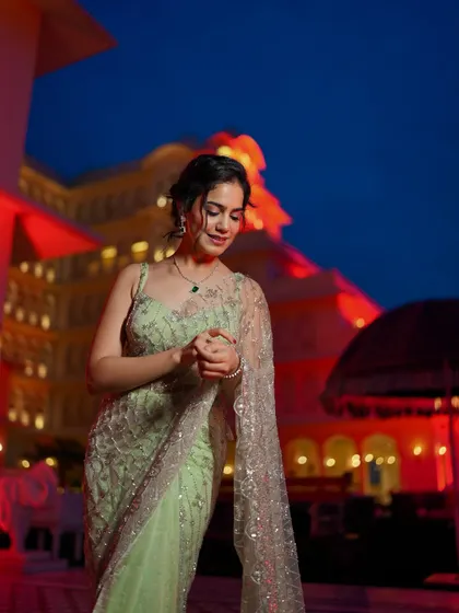 A candid shot looking down, showcasing the intricate sequin work on the saree against the backdrop of a lit-up palace.