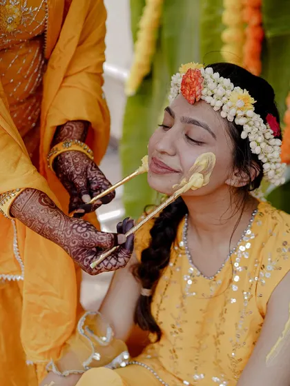 A serene moment as the bride receives the Haldi paste. The floral jewelry and intricate henna on the hands add beautiful detail to the shot.