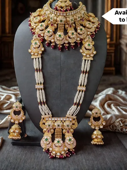 This magnificent bridal set, available for purchase, combines a detailed choker with a matching rani haar. The design features traditional motifs with green and red stones, set against strands of white pearls.