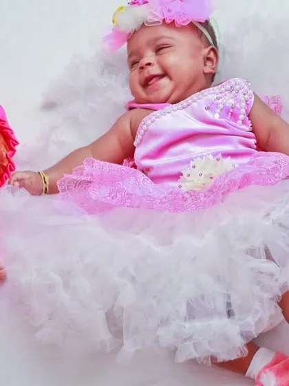 A delightful themed baby photoshoot with a baby girl in a frilly pink dress lying next to a matching doll. We use creative props and outfits to create fun and memorable portraits.