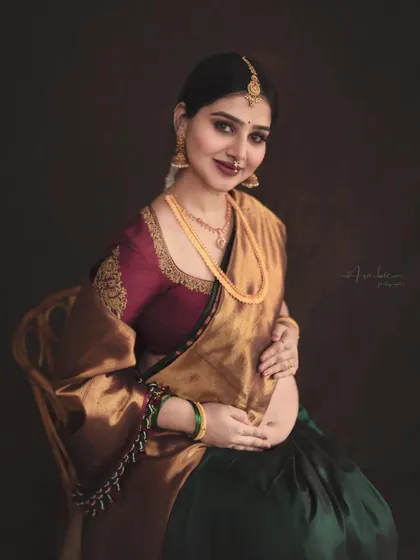 This portrait is a celebration of Indian heritage, featuring a mother-to-be in a stunning Kanjeevaram silk saree with intricate blouse embroidery. The warm, moody lighting and classic pose create a timeless, painterly effect.
