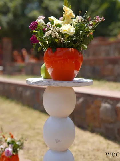A quirky and modern decor piece. This unique white pedestal with its spherical design holds a bright orange vase, showcasing our ability to mix contemporary elements into any theme.