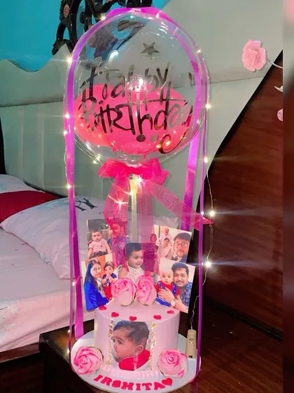 This is my signature balloon cake bouquet, perfect for making a big impression. For this order, I created a custom pink eggless cake featuring the birthday girl's photo, surrounded by a collage of family pictures. The entire display is wrapped in fairy lights and topped with a personalized "Happy Birthday" balloon.