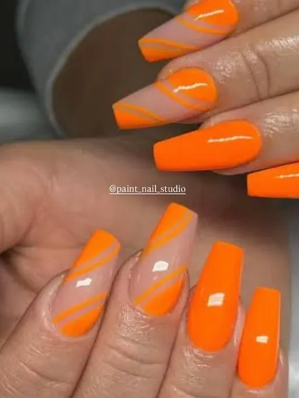 A bold and graphic summer look. This design features bright, solid orange nails paired with accent nails that have orange swirls on a clear base.