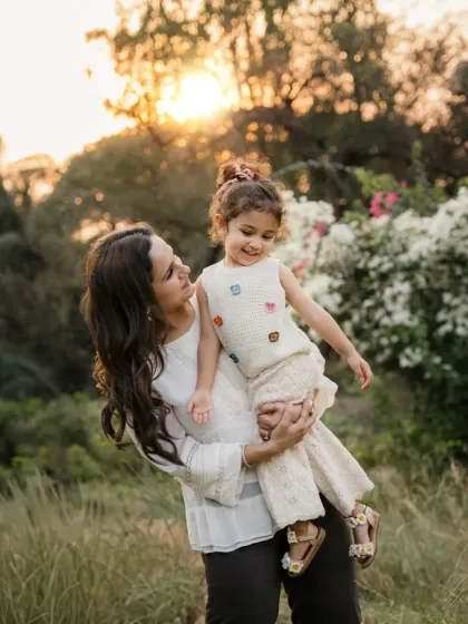 A mother holds her daughter against the warm glow of the setting sun. This outdoor portrait is filled with warmth and affection.