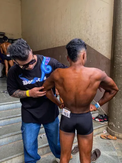 Adjusting a client's back pose backstage. Proper posing highlights muscle groups and hides any weaknesses.