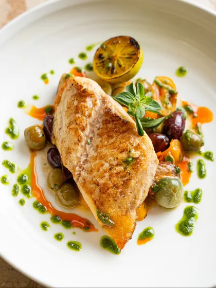 A beautifully plated pan-seared fish with olives and a pesto drizzle. This clean, bright style of food photography is ideal for modern European restaurant menus.