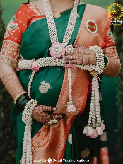A close-up of the floral kamarband, a beautiful way to adorn the baby bump. The 'Aai' brooch is a special, customized touch.