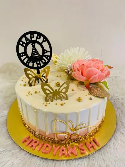 A simple yet elegant butterfly cake with a white drip, topped with a pink flower and golden butterflies.