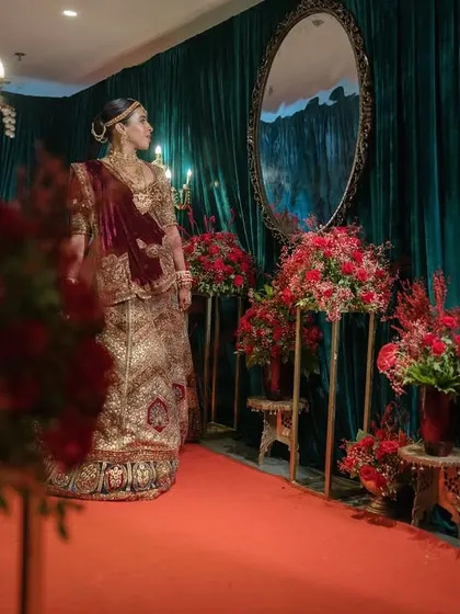 A bride stands against a backdrop of rich emerald velvet drapes and red floral accents. The decor is designed to complement and enhance the bridal attire, creating picture-perfect moments.