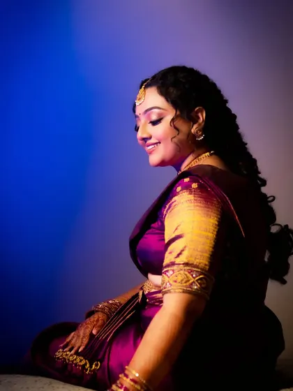 A beautiful side-profile portrait of a bride in a purple saree, smiling contentedly.