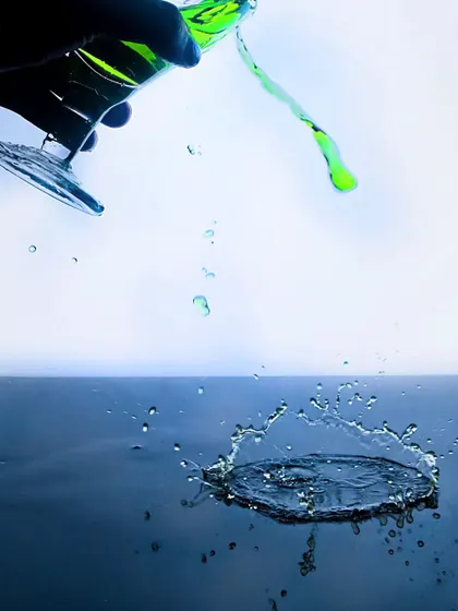 A creative splash shot where a green liquid is being poured from a tilted glass, creating a dynamic splash below. This abstract and artistic shot is great for a bold campaign.