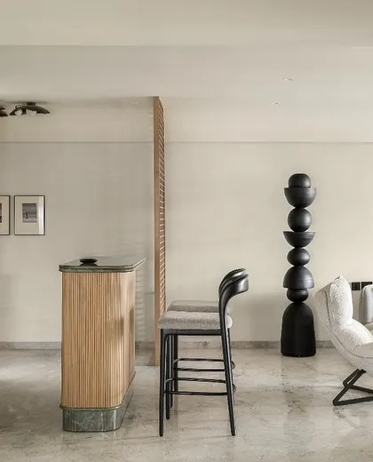 This view showcases the bar and living area of the Noir Blanc House. The design features a black totem sculpture and a custom bar with green marble, creating distinct zones that are visually connected through a shared palette of sophisticated materials.