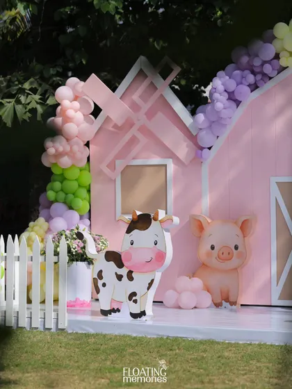 A closer look at the main barnyard backdrop. Our custom-made cow and pig characters stand cheerfully in front of the pink barn, surrounded by pastel balloon garlands, making for a perfect birthday photo spot.